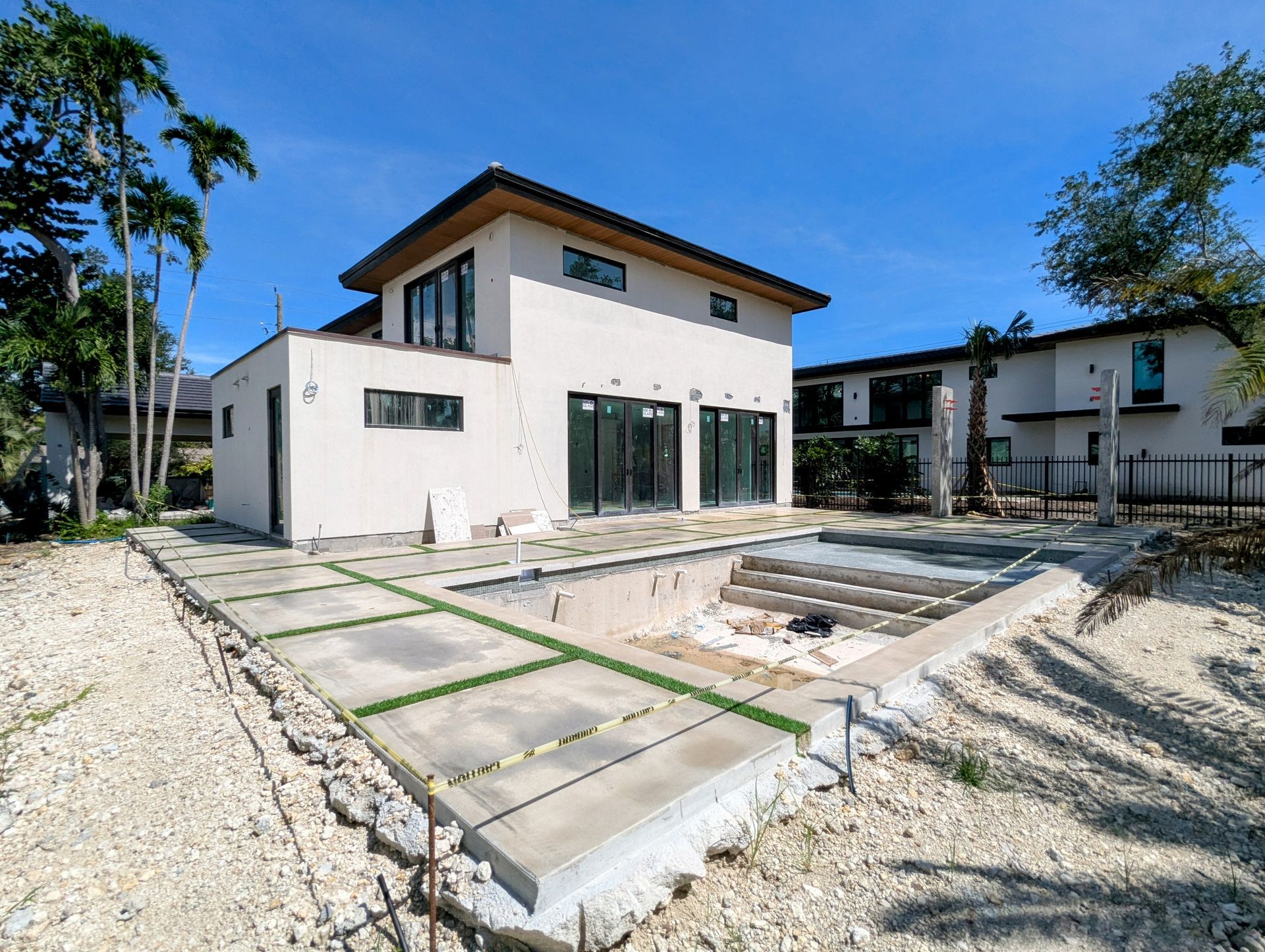Modern two-story house under construction with a planned pool area, surrounded by gravel and trees.