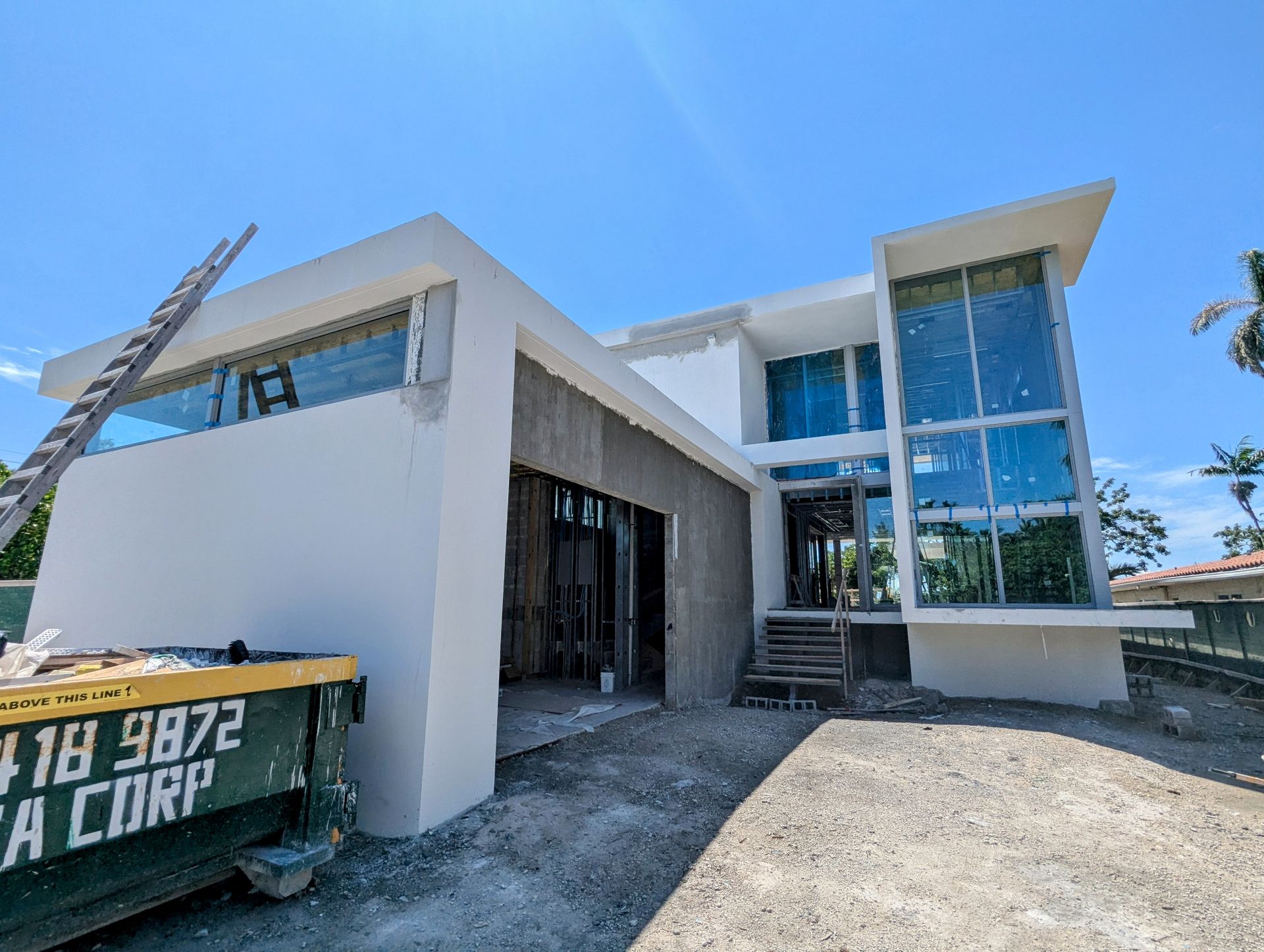 A large white house is being built with a dumpster in front of it.