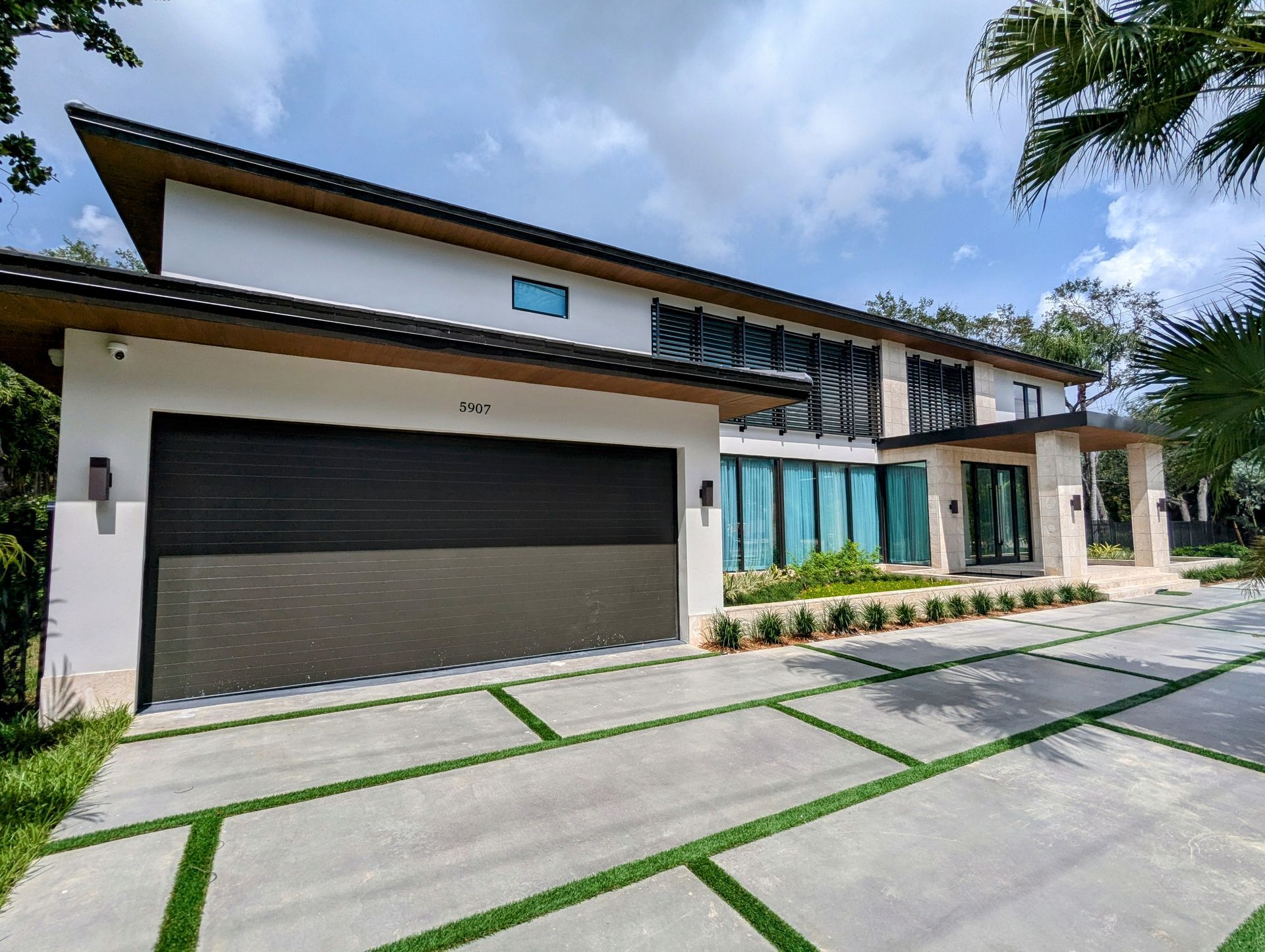 Modern white two-story house with black garage door, concrete driveway, and lush landscaping.