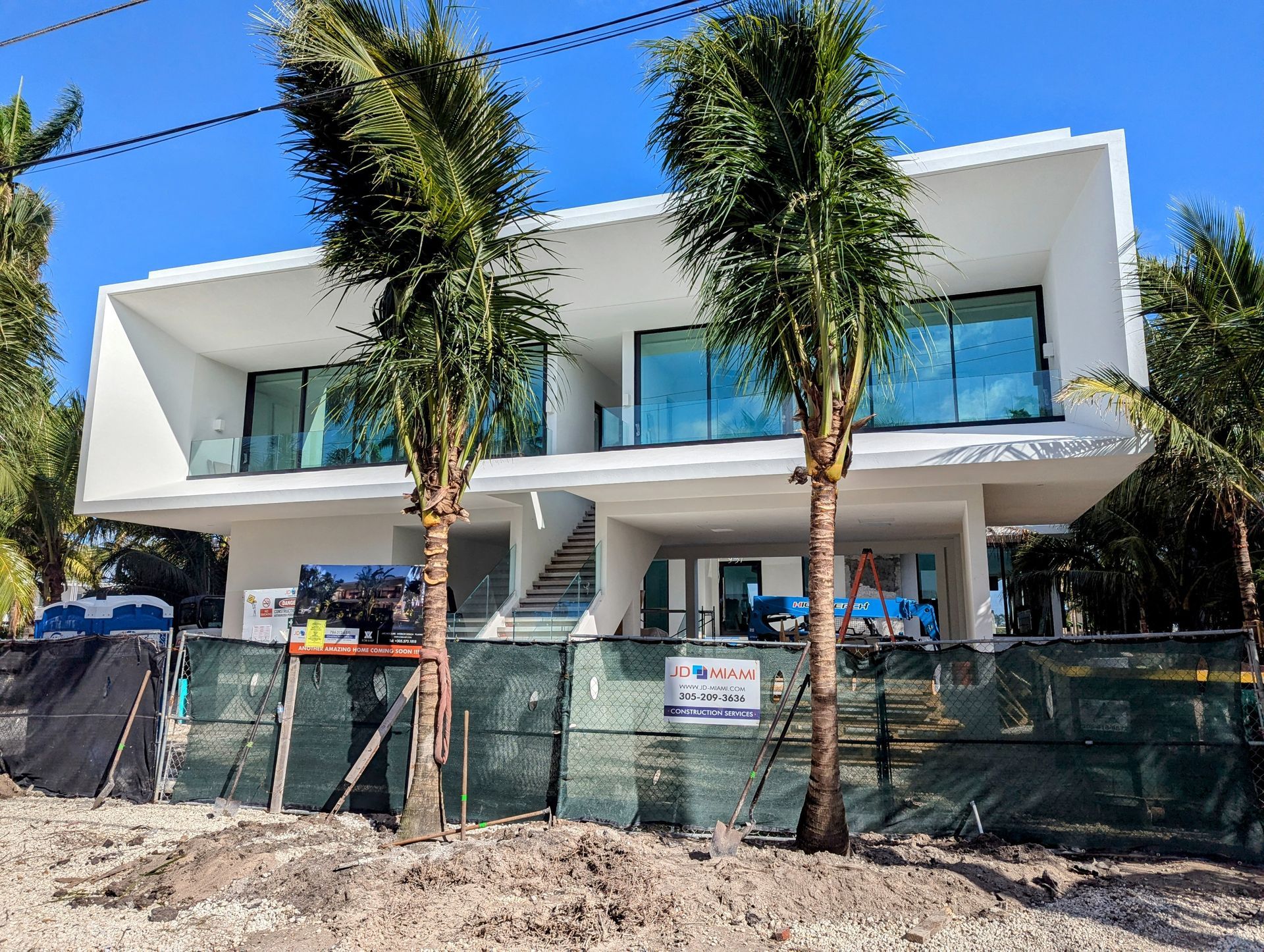 A large white house is under construction with palm trees in front of it.