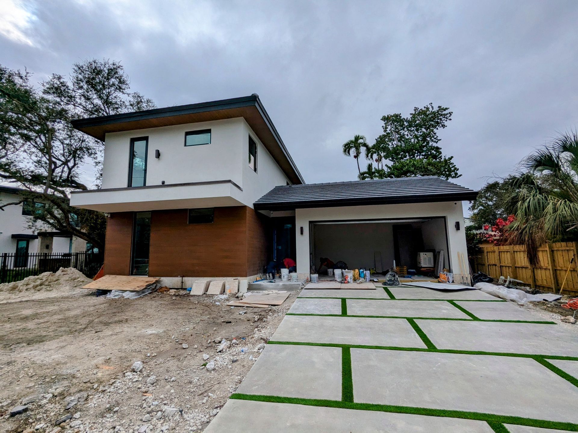 Modern two-story house under construction with a gray driveway and green artificial grass accents.