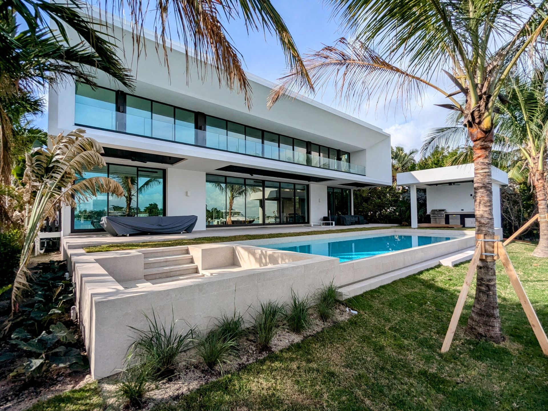 A large white house with a swimming pool in the backyard surrounded by palm trees.