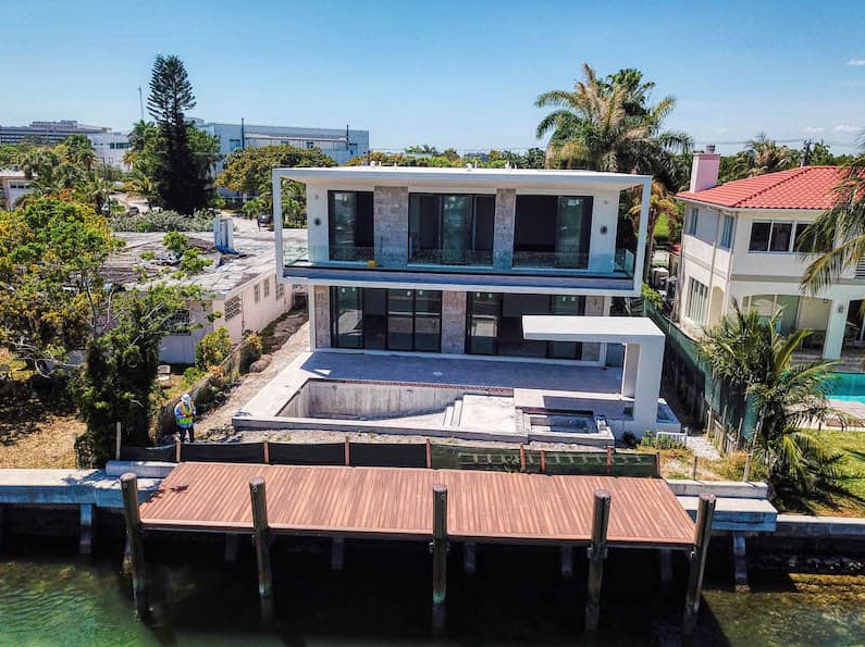 Modern waterfront house with dock, large windows, and a partially built-in pool.