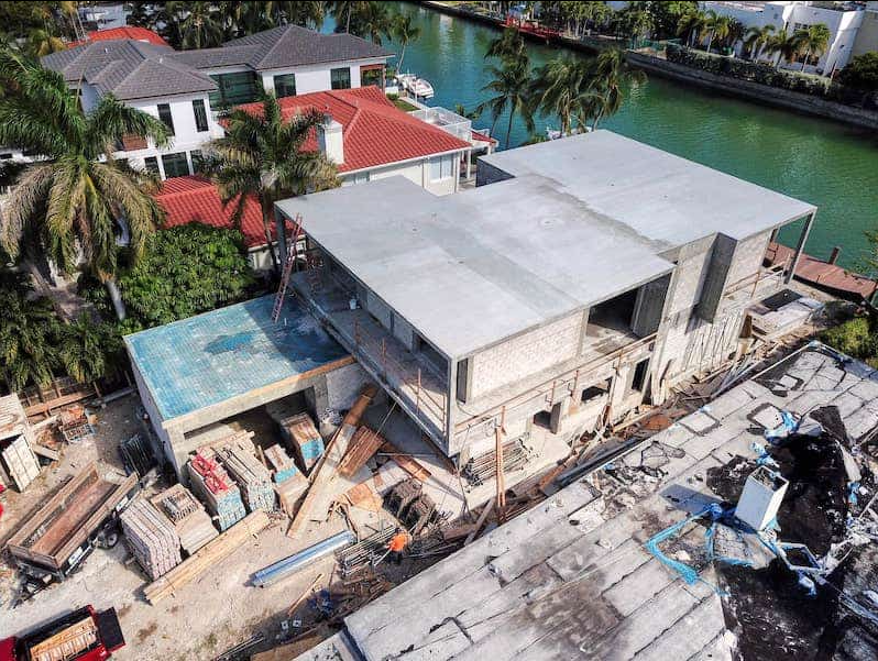 Construction of a house on a waterway. Gray concrete structure with exposed beams and building materials.