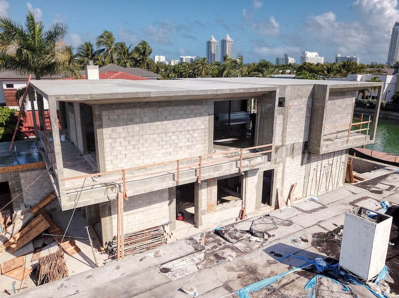 House under construction, unfinished concrete structure, Miami. Construction materials and water nearby.