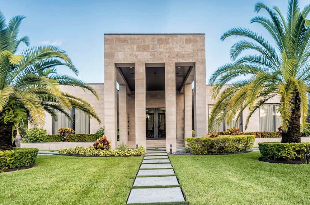 Modern home exterior with stone facade, columns, palm trees, and manicured lawn.