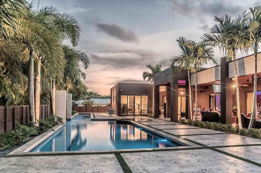 Modern home with pool, palm trees, and dusk sky.