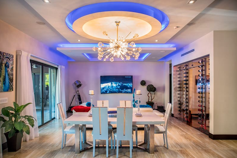 Modern dining room with a white table, chandelier, and built-in wine rack.