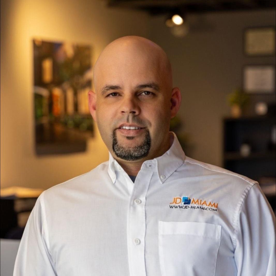 Man with a goatee wearing a white button-down shirt with a company logo.