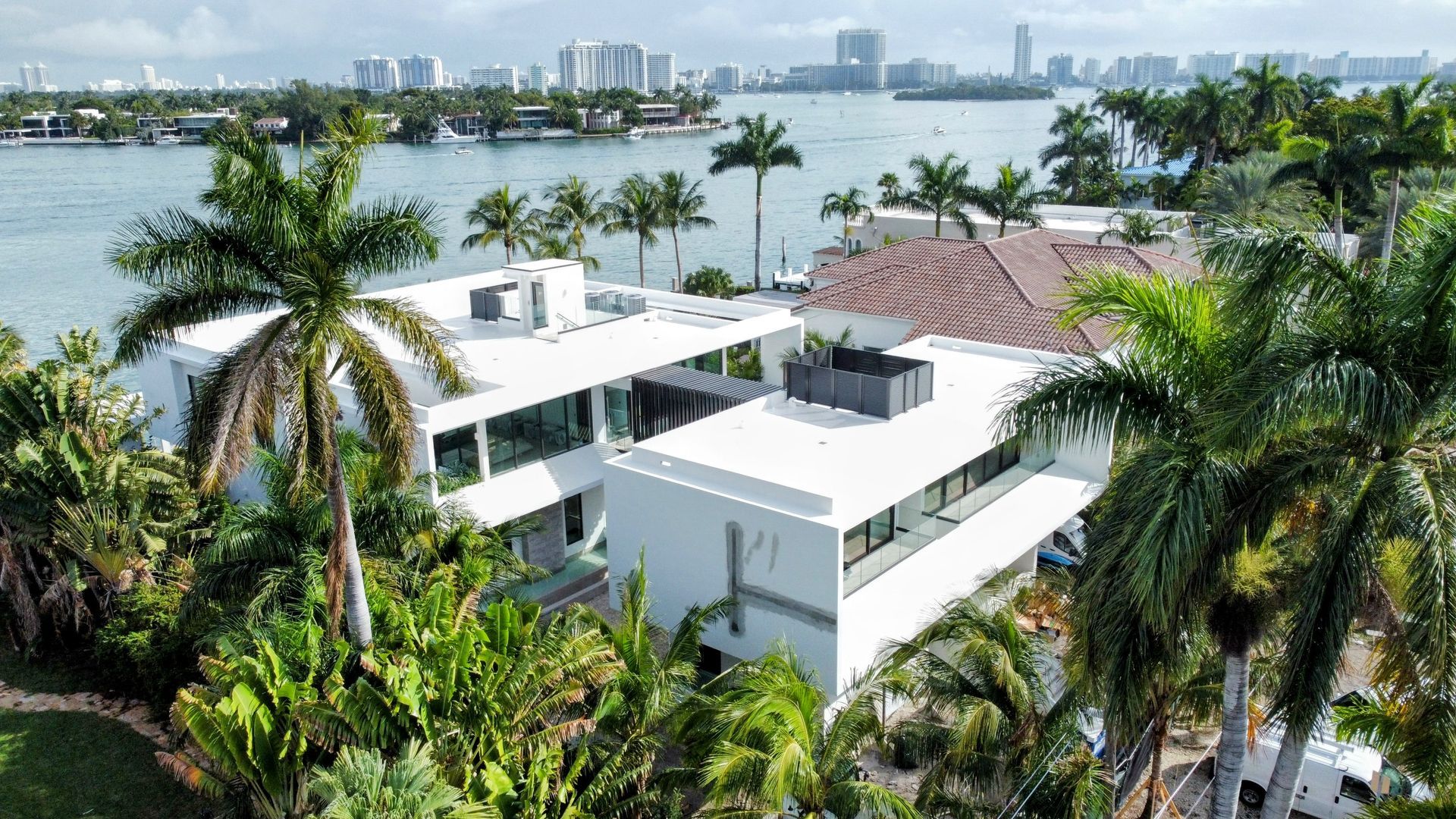An aerial view of a large white house surrounded by palm trees next to a body of water.