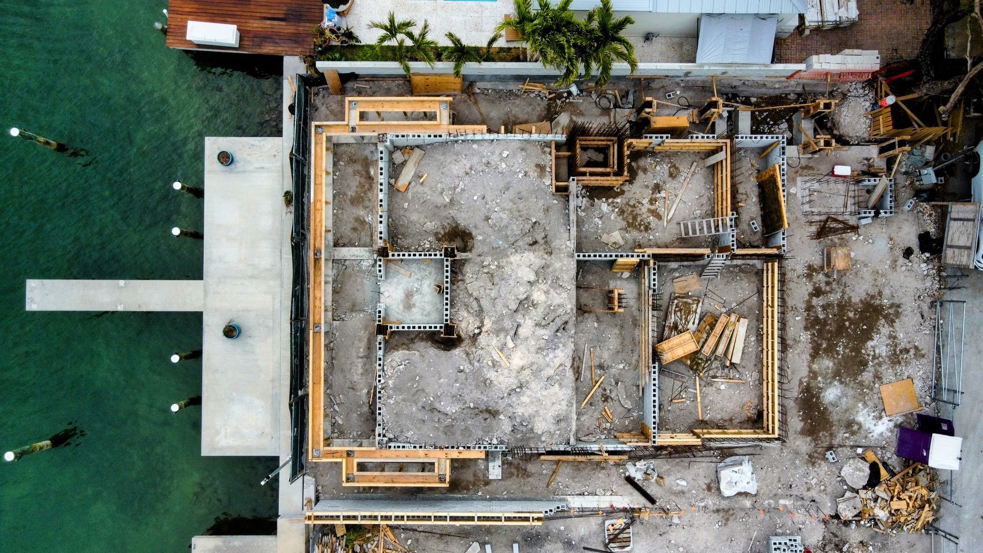 Aerial view of a building foundation under construction next to a body of water and a pier.