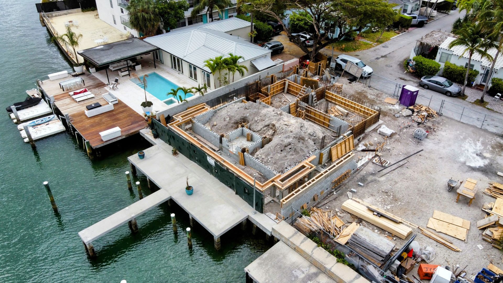 Aerial view of a construction site next to a dock and waterfront homes.