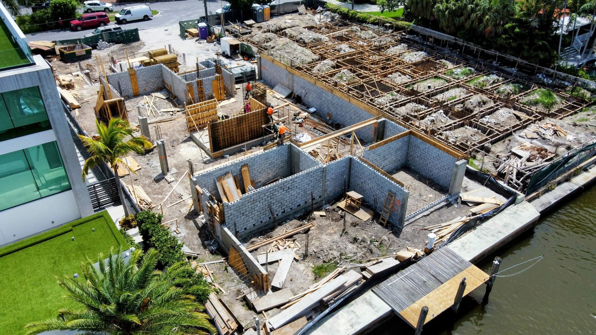 Aerial view of a construction site with concrete foundation walls, wooden framework, and surrounding buildings.