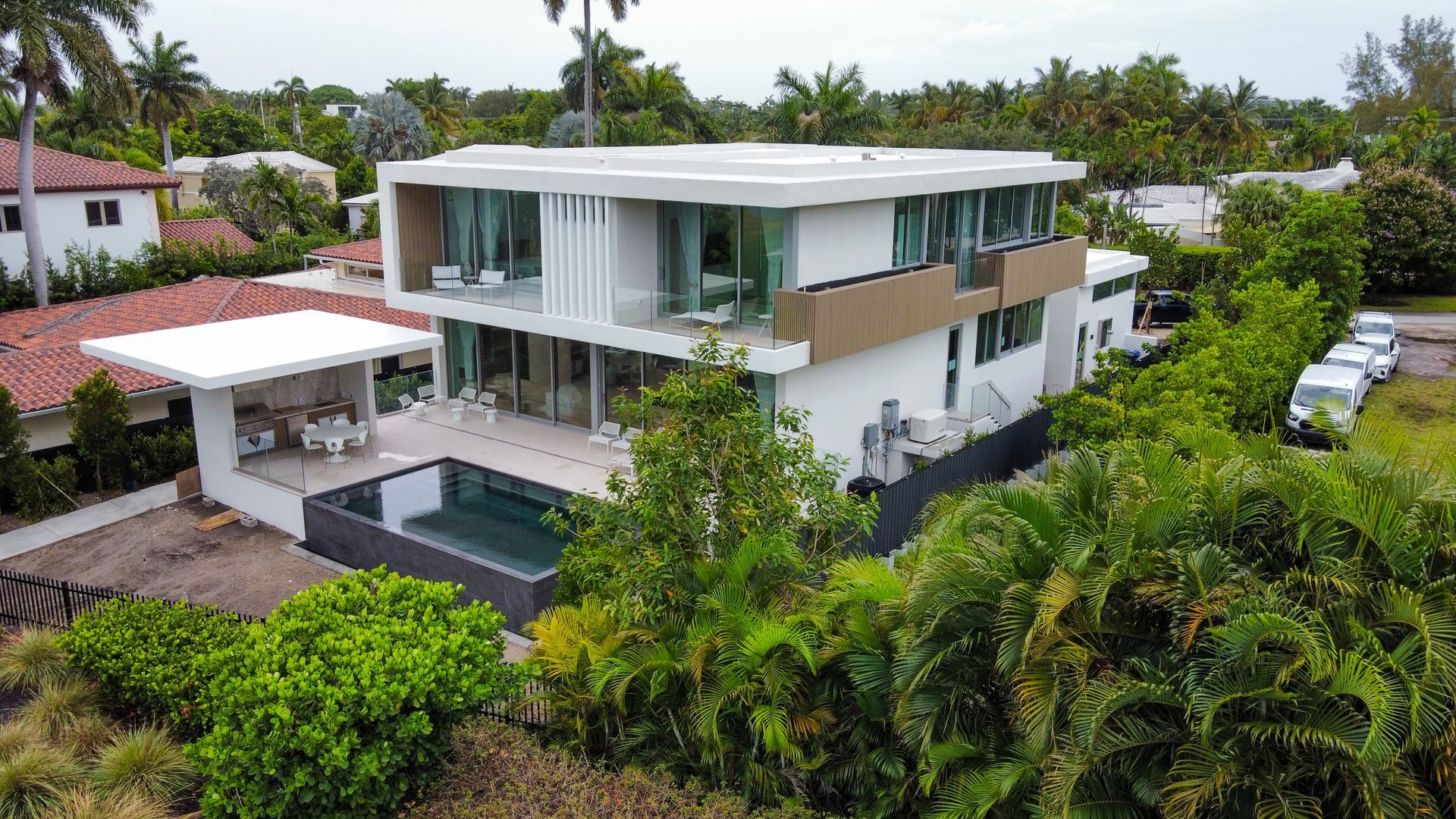 Modern white house with a pool, glass walls, and a flat roof in a tropical setting.