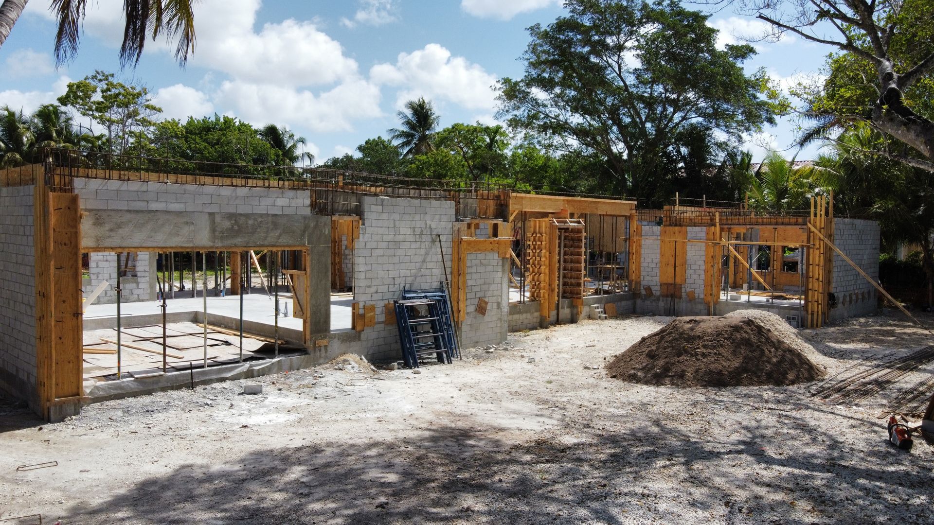 Construction site; unfinished building with concrete and wooden supports, dirt ground, blue sky.