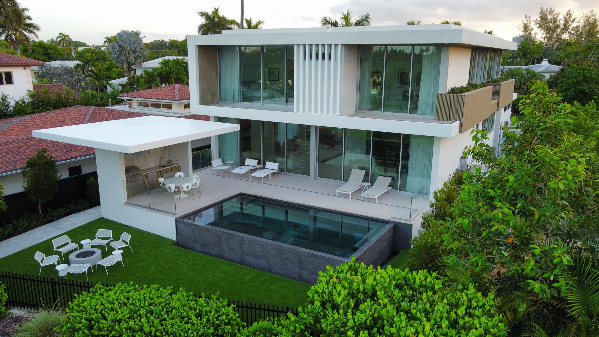 Modern two-story house with a pool, patio, and green lawn, surrounded by lush trees.