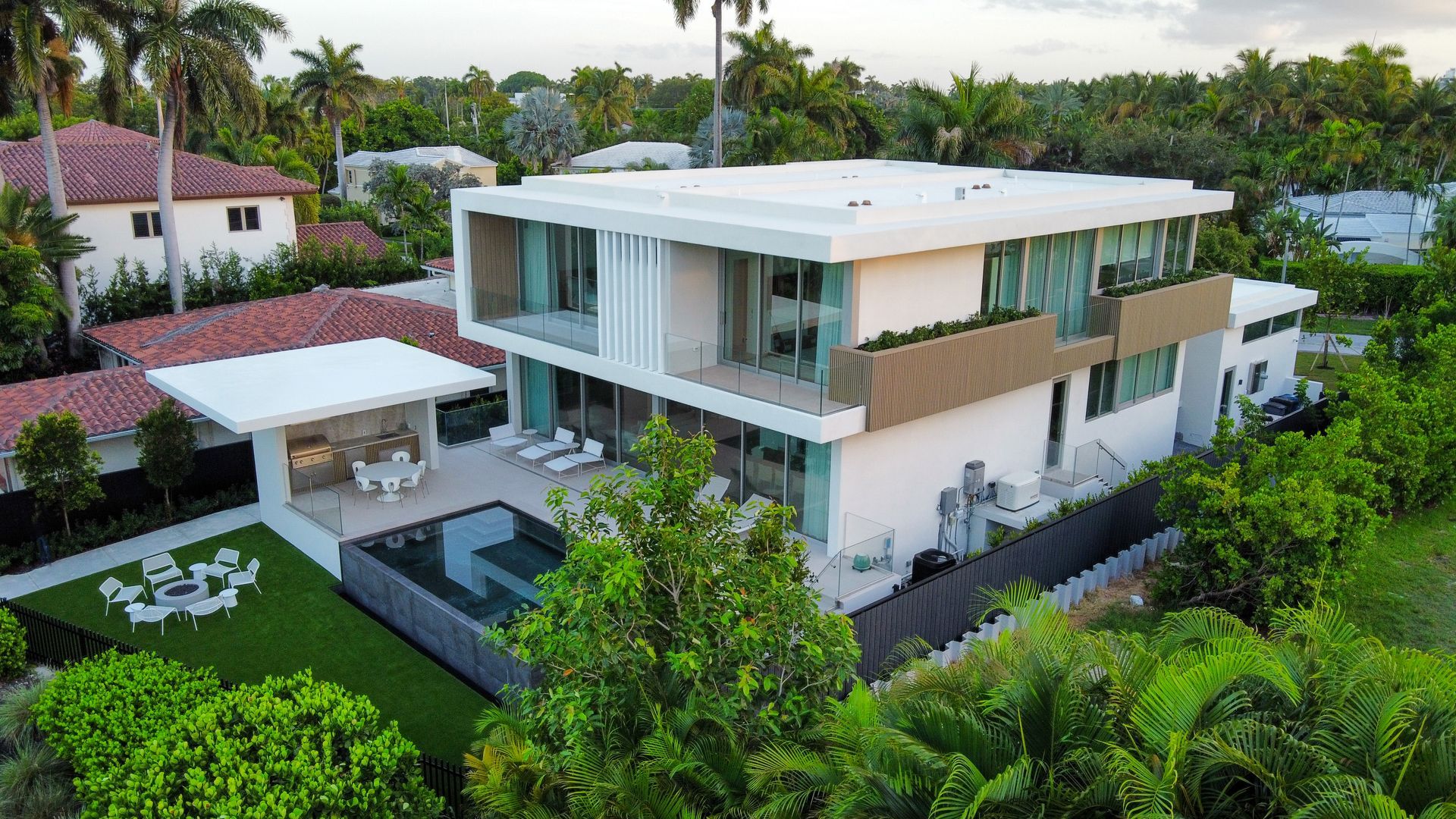 Modern white house with a pool and patio, surrounded by lush greenery, in a suburban setting.
