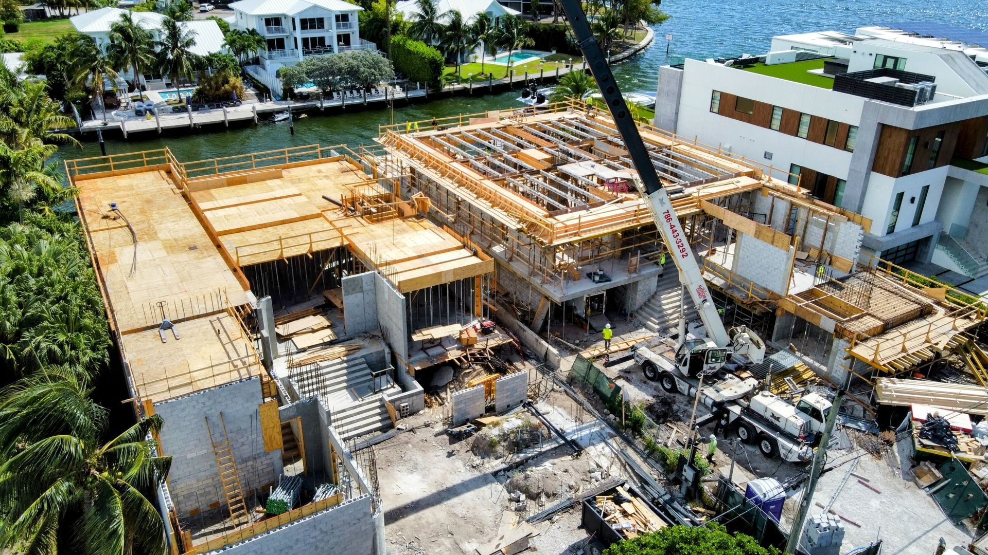 Construction of a large house with a crane, overlooking a waterway.