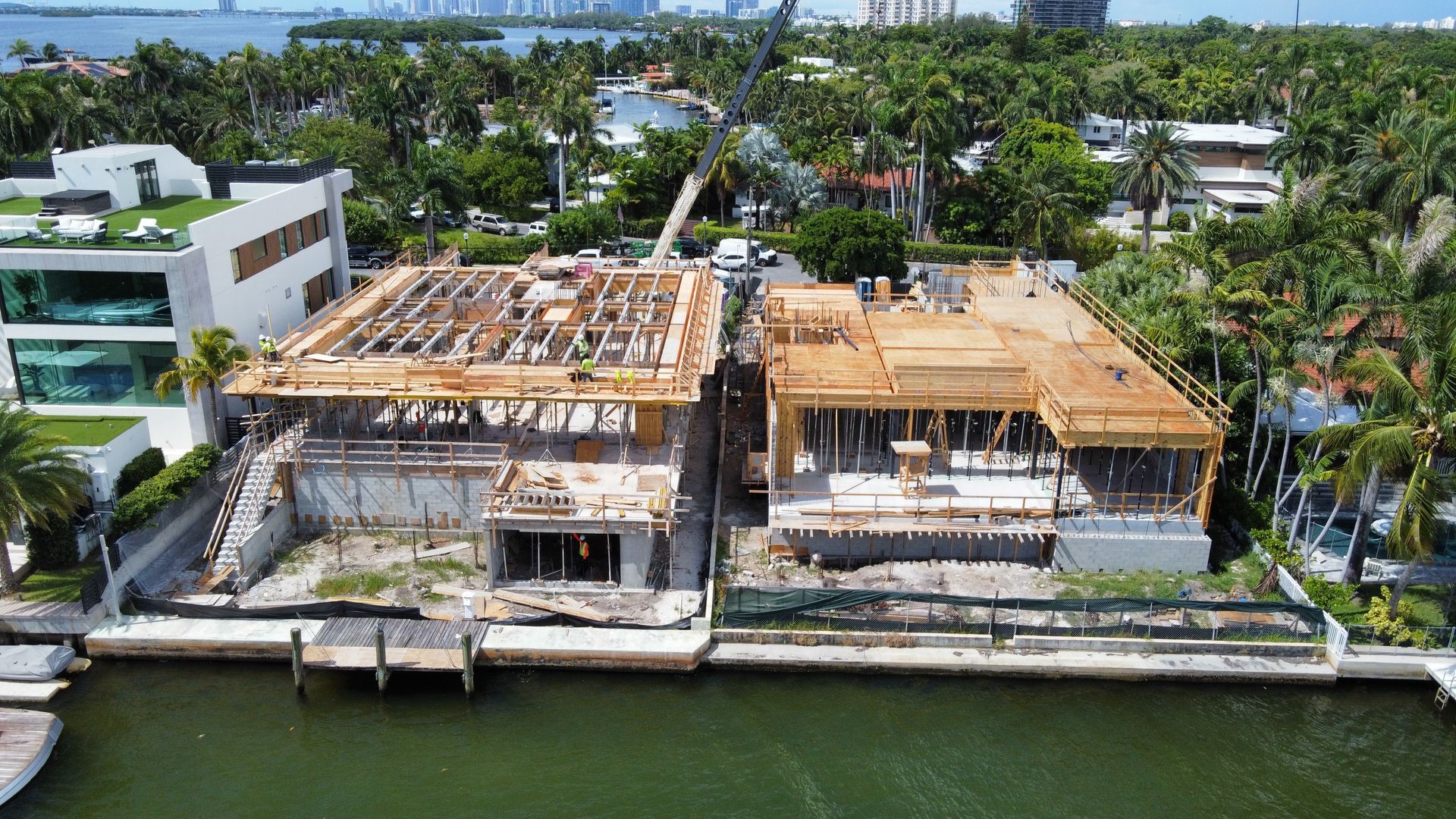 Aerial view of two waterfront homes under construction; wood frames, dock.