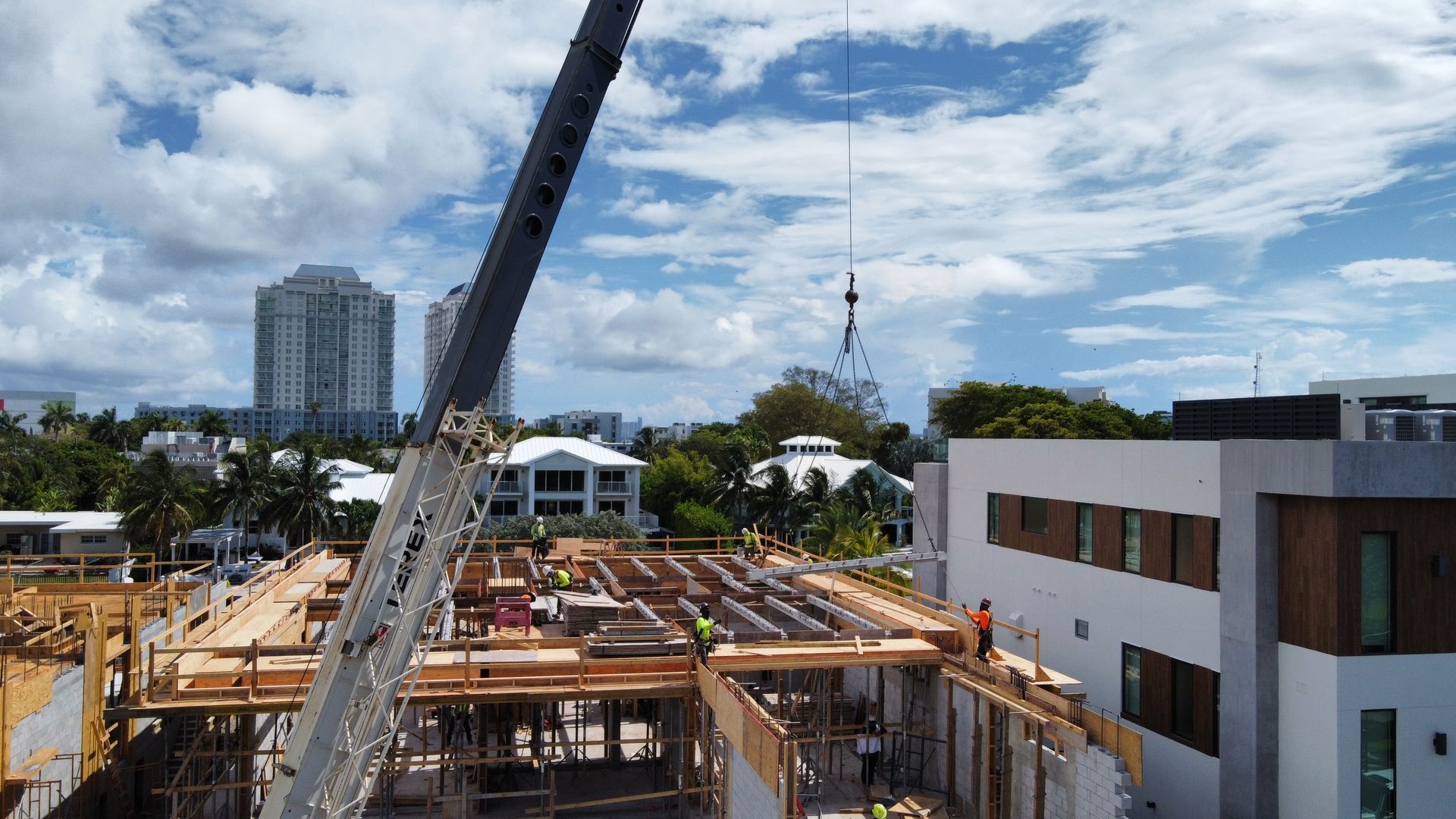 Construction site with crane lifting material; workers on wooden frame buildings under cloudy sky.