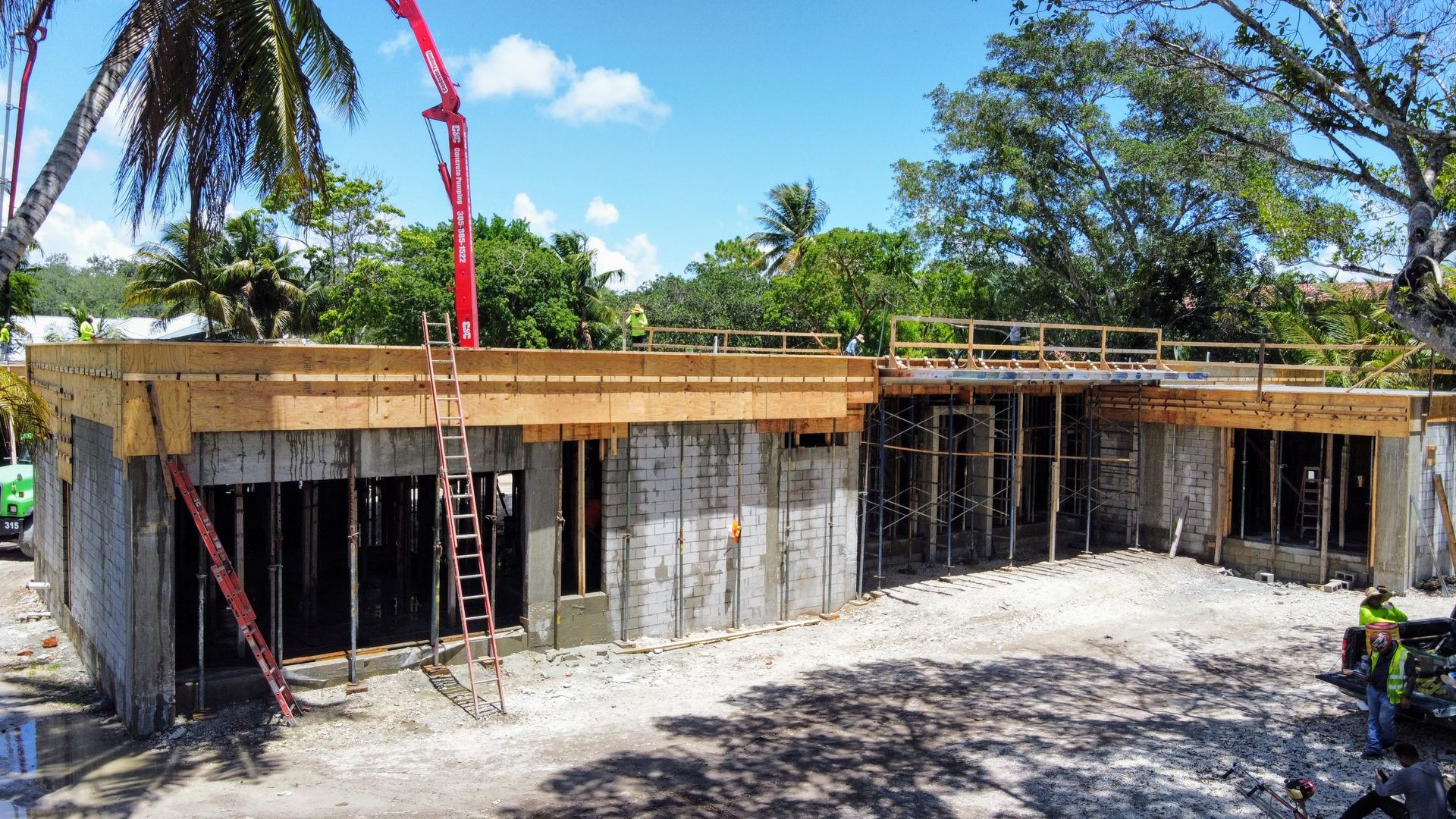 Construction site of a concrete building; concrete being poured by a red boom pump, set in a tropical environment.