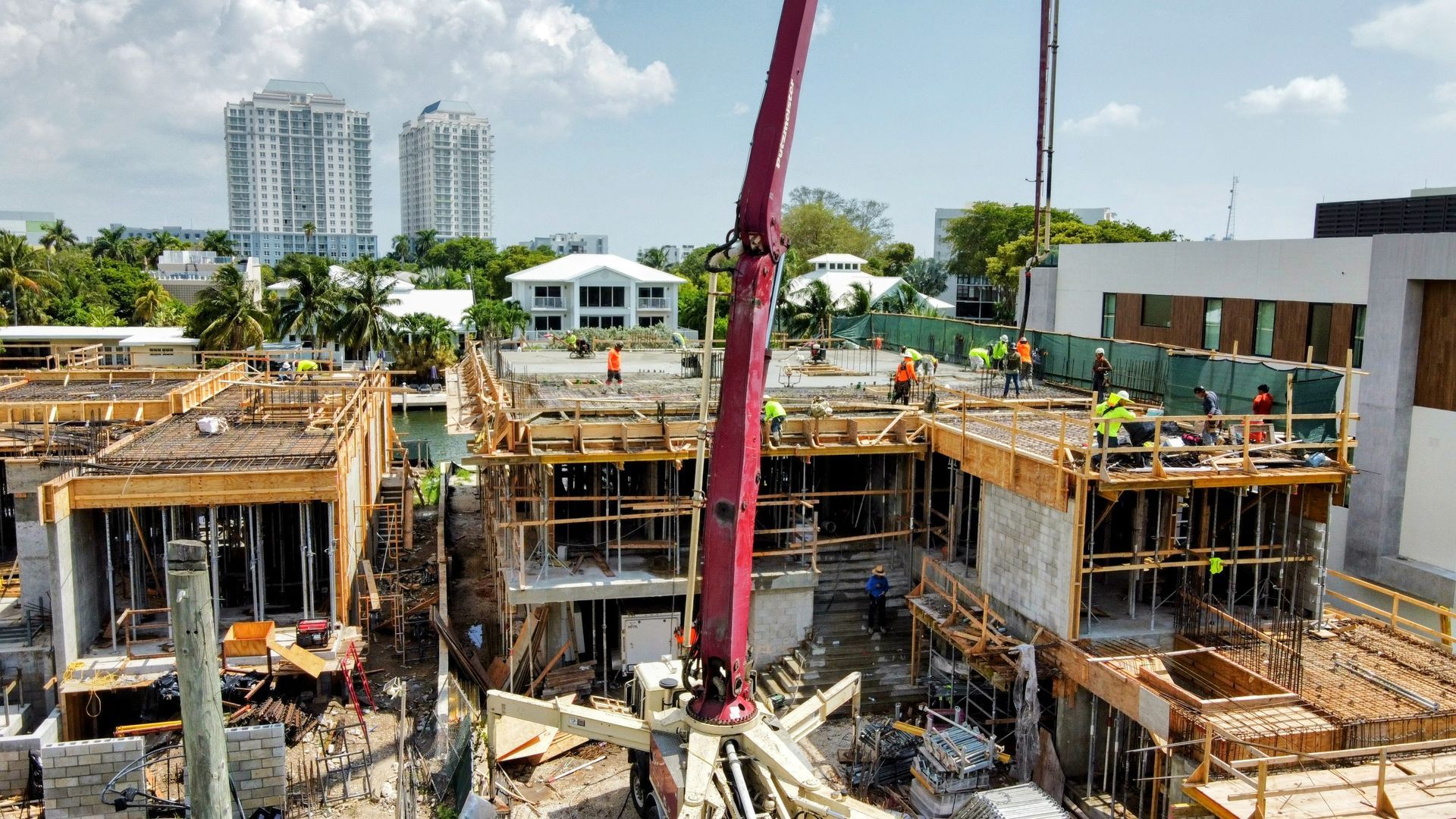 Construction site: Crane pouring concrete on multi-story buildings; workers in safety vests. City backdrop.