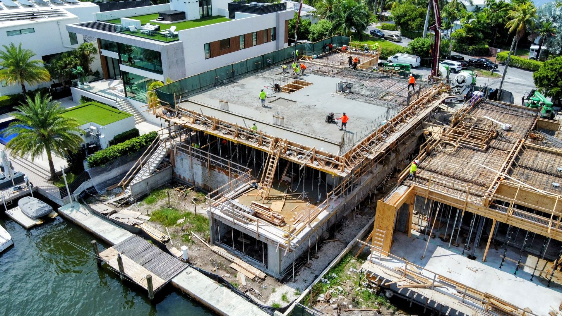 Construction site of a waterfront house, concrete forms and workers visible.