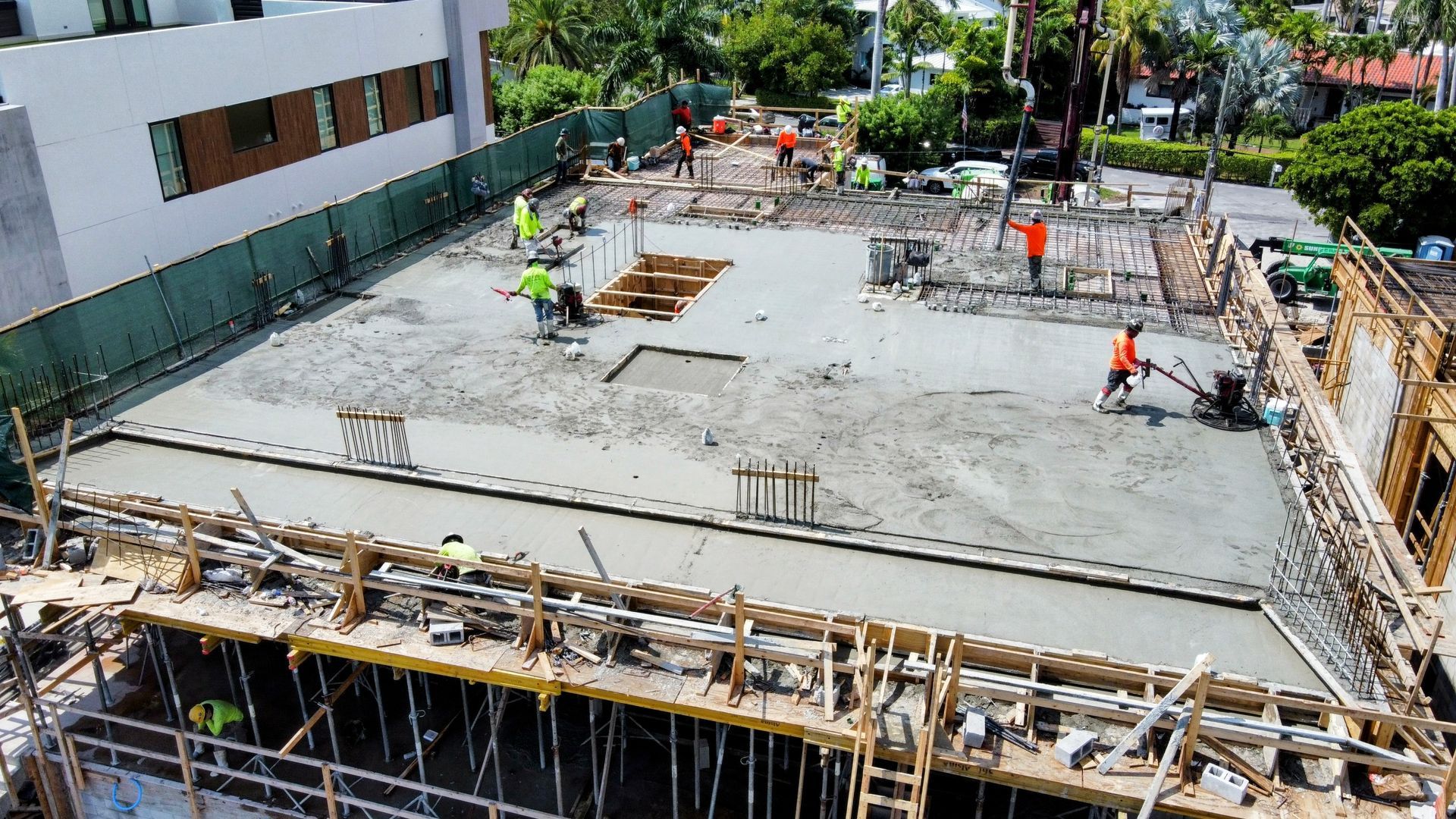 Construction site with workers pouring and leveling concrete on a rooftop deck; sunny day.