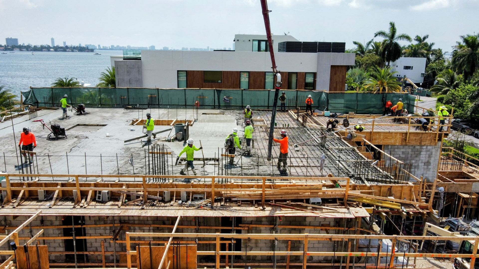 Construction site with workers pouring concrete; ocean and building in background.