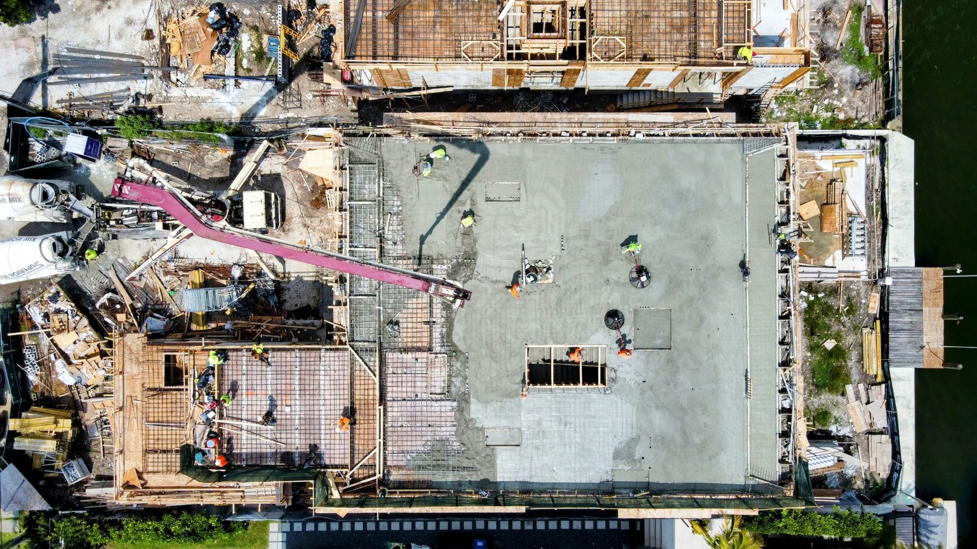 Construction site from above; workers, concrete, wood frames, and equipment.