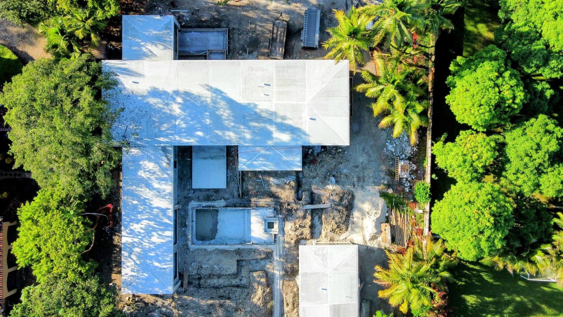 Overhead view of a building under construction, surrounded by trees. The roof has a silver covering.