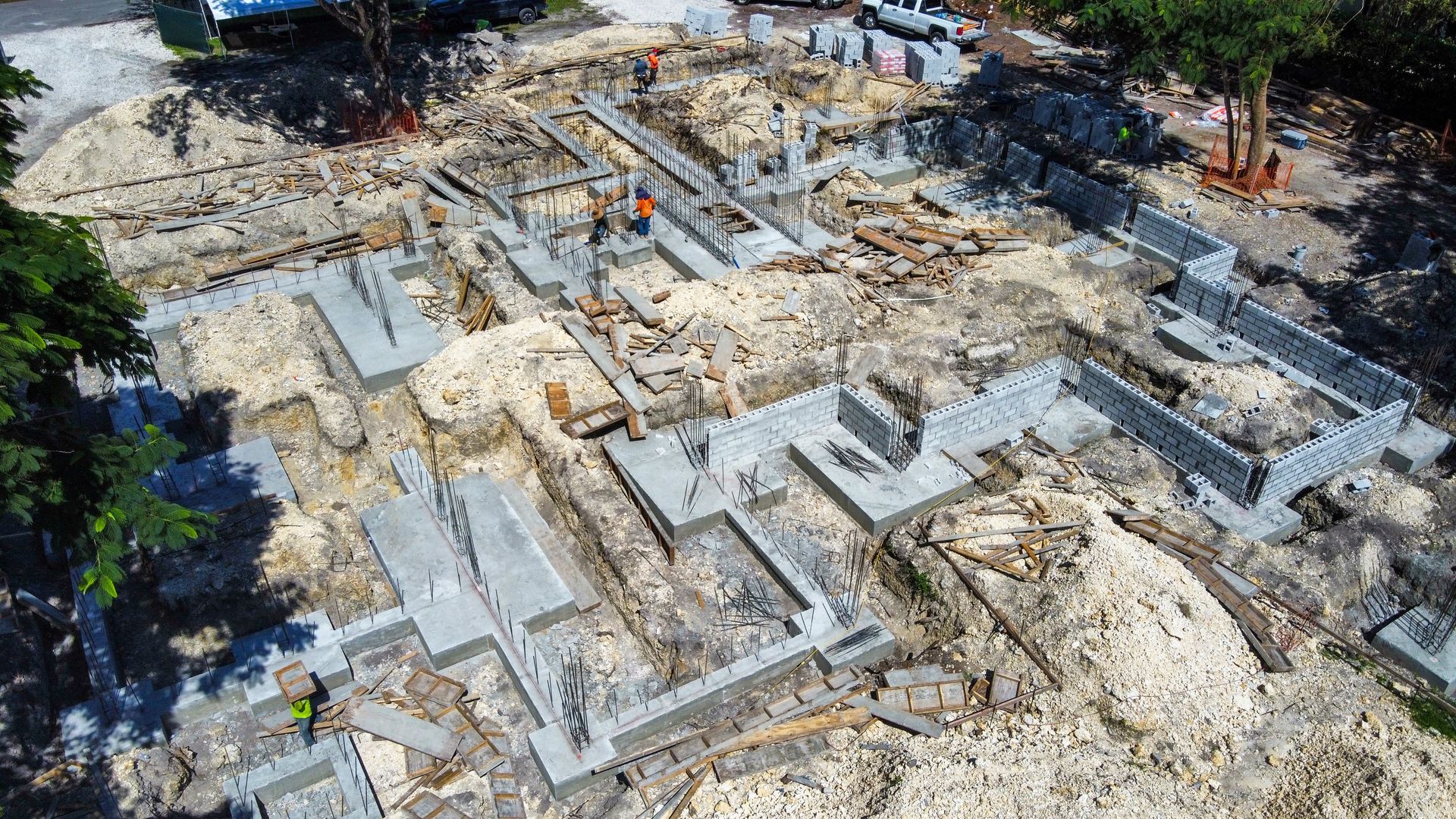 Construction site with concrete foundations and footings, dirt, and workers.