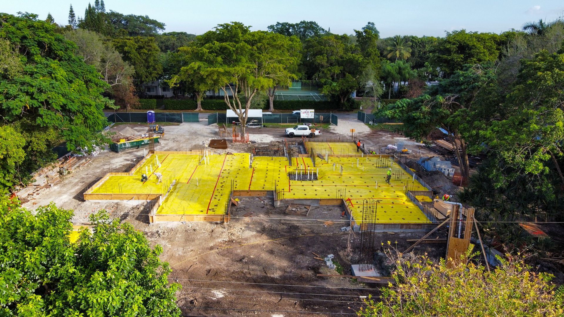 Construction site with yellow foundation, surrounded by trees.