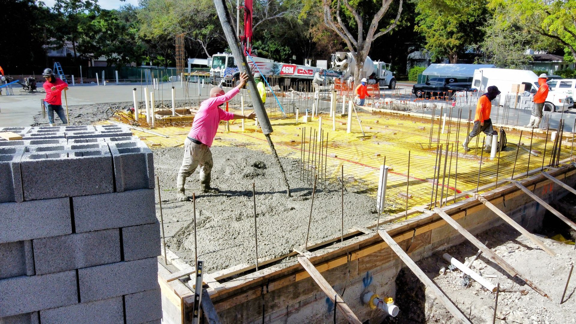 Construction workers pour concrete at a construction site. Concrete block walls are partially built.