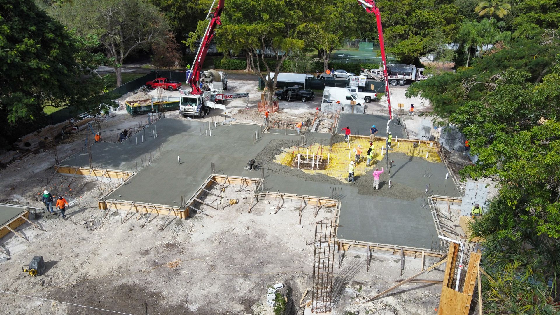Construction site with concrete pouring, showing foundation and trucks.