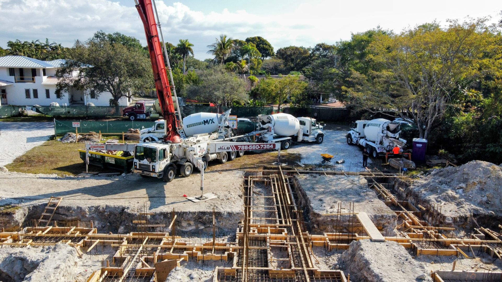 Construction site with concrete trucks and pump pouring concrete into wooden forms.
