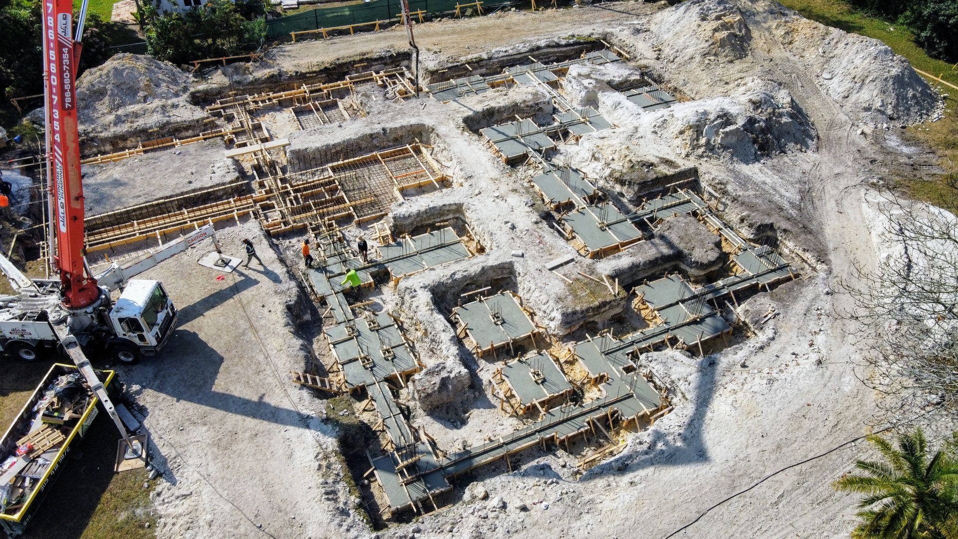 Construction site aerial view; foundations and a crane, dirt and workers visible.
