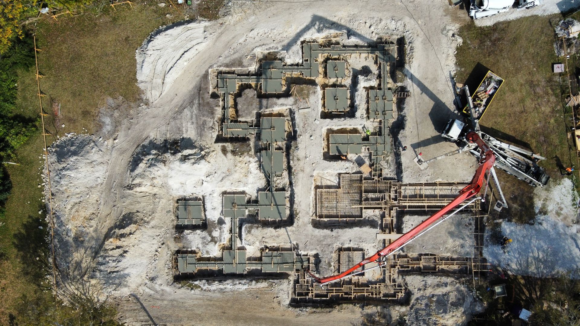 Aerial view of a construction site. Concrete foundation being poured into forms with a pump truck extending a red hose.