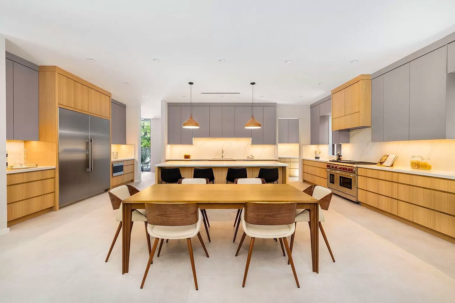 Modern kitchen with light wood cabinets, gray upper cabinets, stainless steel appliances, and a dining table.