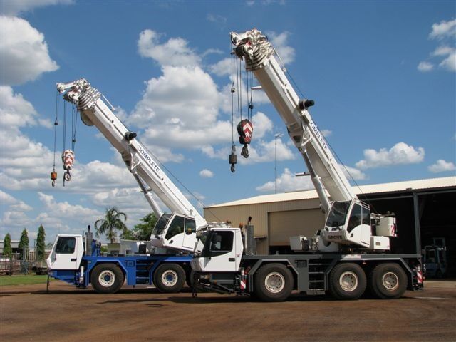 Two large mobile cranes with extended booms and heavy tyres parked outside a workshop