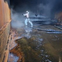 A man in a protective suit is cleaning a tank with a hose.