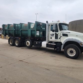 A white roll off truck with a green trailer is parked in a parking lot.