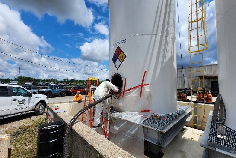 A man is cleaning inside a white tank with a hazard symbol on it.