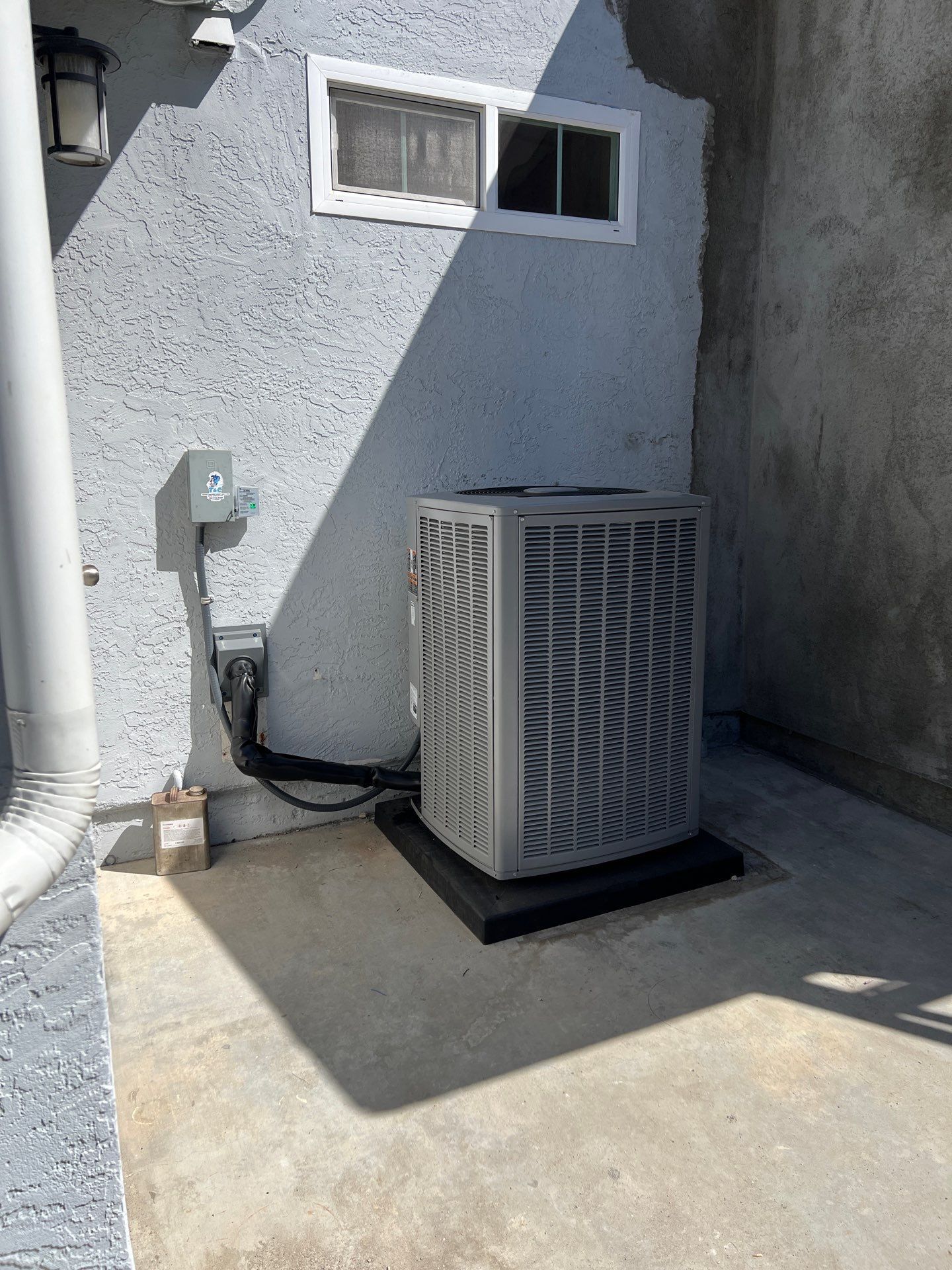 Outdoor air conditioning unit on a concrete slab, next to a stucco wall and window.