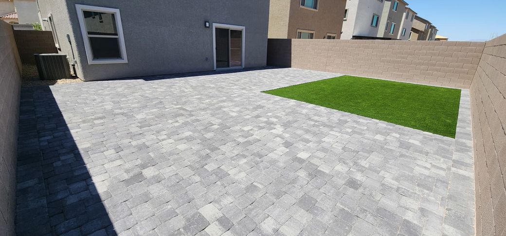 Backyard patio with gray pavers and a small patch of green turf.