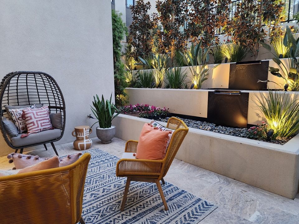 Patio with tiered fountain, lounge chairs, plants, and accent lighting.