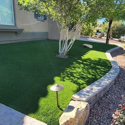 Green artificial grass lawn with tree, low wall, and outdoor lamp.