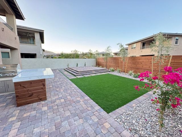 Backyard with brick patio, artificial grass, wooden steps, and a grill area.