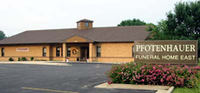The Pfotenhauer Funeral Home East building with a tan brick exterior, brown roof, and a sign in the foreground.