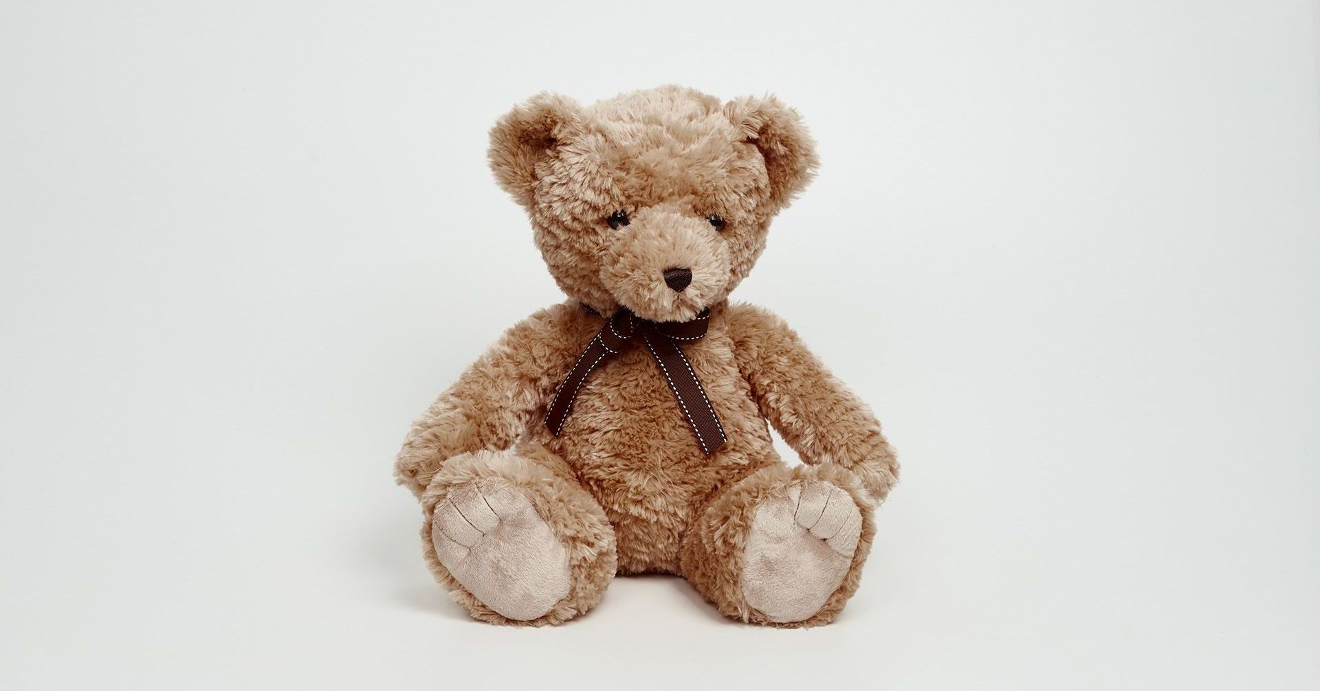Brown teddy bear with a dark ribbon, sitting on a white background